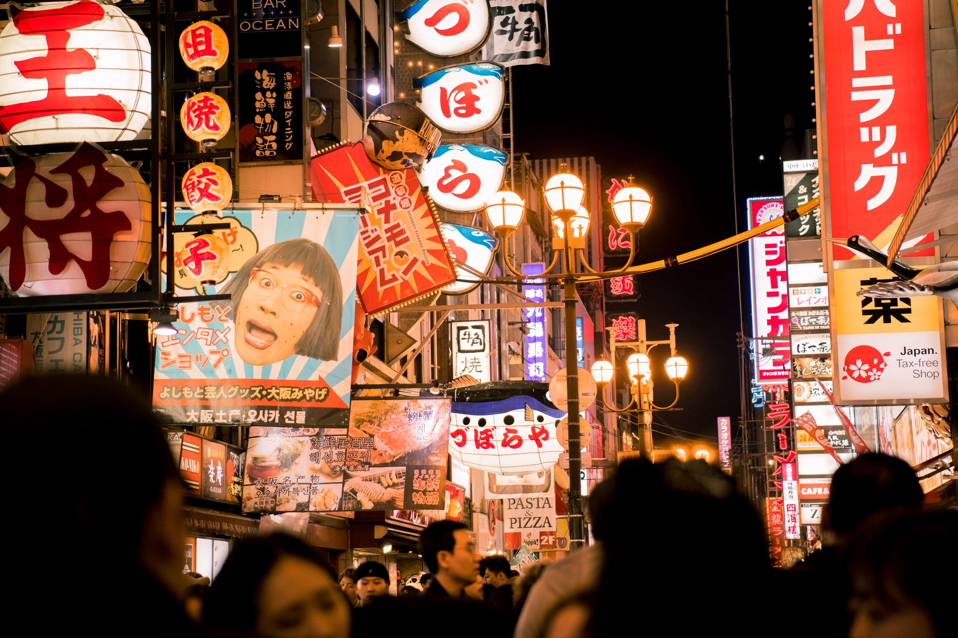 Vibrant daytime scene of Dotonbori's famous food street with colourful stalls, neon signs, and crowds of people eating and shopping