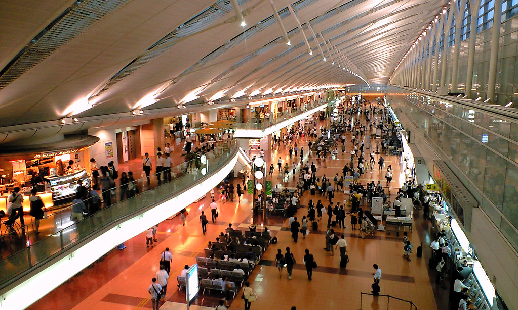 Travelers moving through Haneda Airport arrivals with train signage in the background.