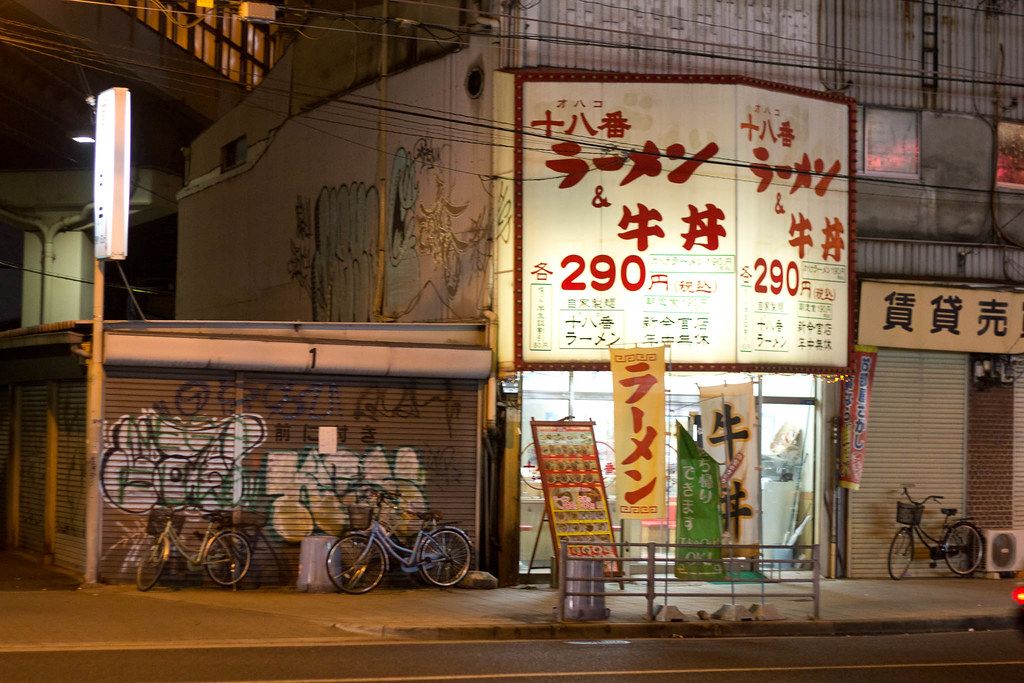 A steaming bowl of ramen on a counter in a busy Osaka night-time shop.